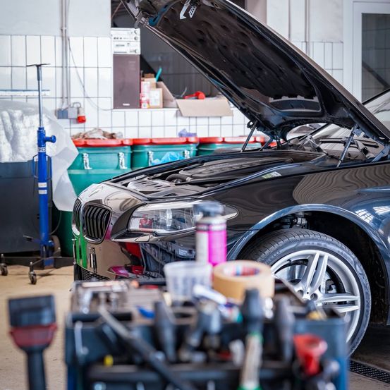 Ein schwarzer BMW-Wagen mit geöffneter Motorhaube in einer Garage, umgeben von Werkzeugen und Ausrüstung.