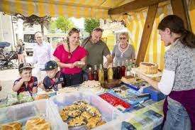 Eine Familie genießt ein Essen unter einem gelb-weißen Zelt, mit mehreren Erwachsenen und Kindern, die um einen Tisch herum versammelt sind, auf dem verschiedene Speisen wie Brot, Gebäck und andere Gerichte stehen.