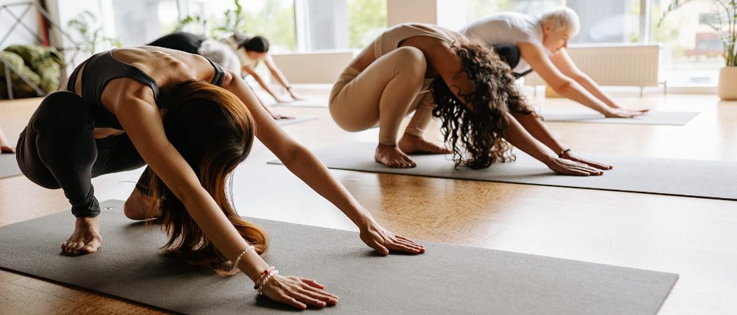 Mehrere Frauen praktizieren Yoga in einem Raum mit großen Fenstern, eine Frau beugt sich rückwärts.