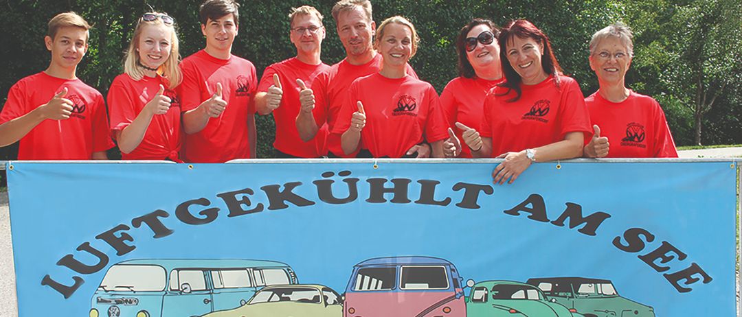 Eine Gruppe von Menschen in roten T-Shirts posiert für ein Foto hinter einem Banner mit Volkswagen-Autos.