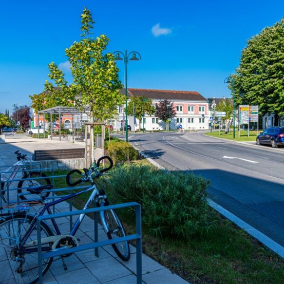 Ein leerer Bürgersteig mit geparkten Fahrrädern, eine Straße mit einem blauen Auto, Gebäuden, Bäumen und Straßenlaternen.