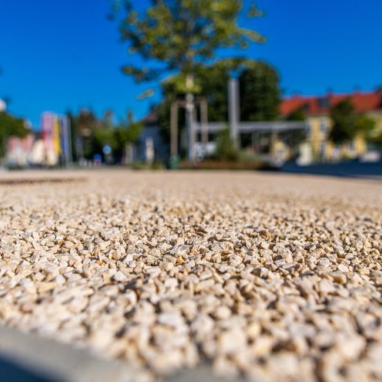 Eine Nahaufnahme von Kies, der eine Straße bedeckt, mit einem unscharfen Hintergrund, der eine Stadt mit Bäumen und Gebäuden zeigt.