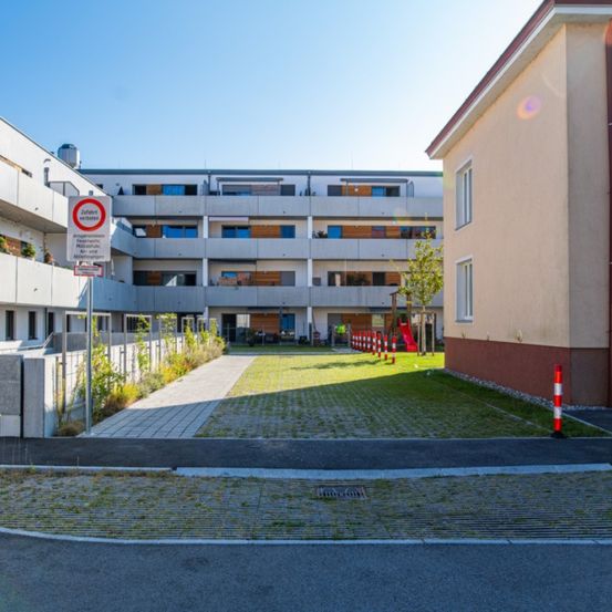 Ein Mehrfamilienhaus mit Spielplatz und Rasen, umgeben von einem Zaun und roten und weißen Stangen.