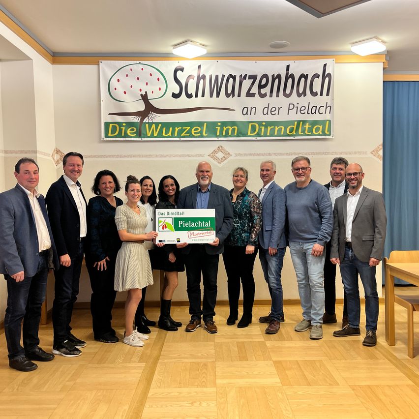 A group of people stand in a room, holding a certificate for Pielachtal. Behind them is a banner with the text Schwarzenbach an der Pielach.