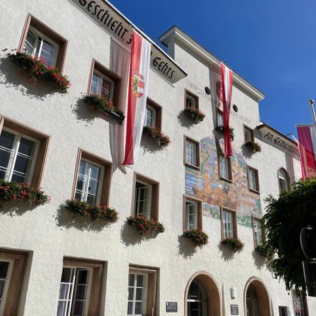 Ein weißes Gebäude mit einem Wandbild und Fahnen mit roten Blumen an jedem Fenstersims