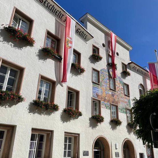 Ein weißes Gebäude mit einem Wandbild und Fahnen mit roten Blumen an jedem Fenstersims