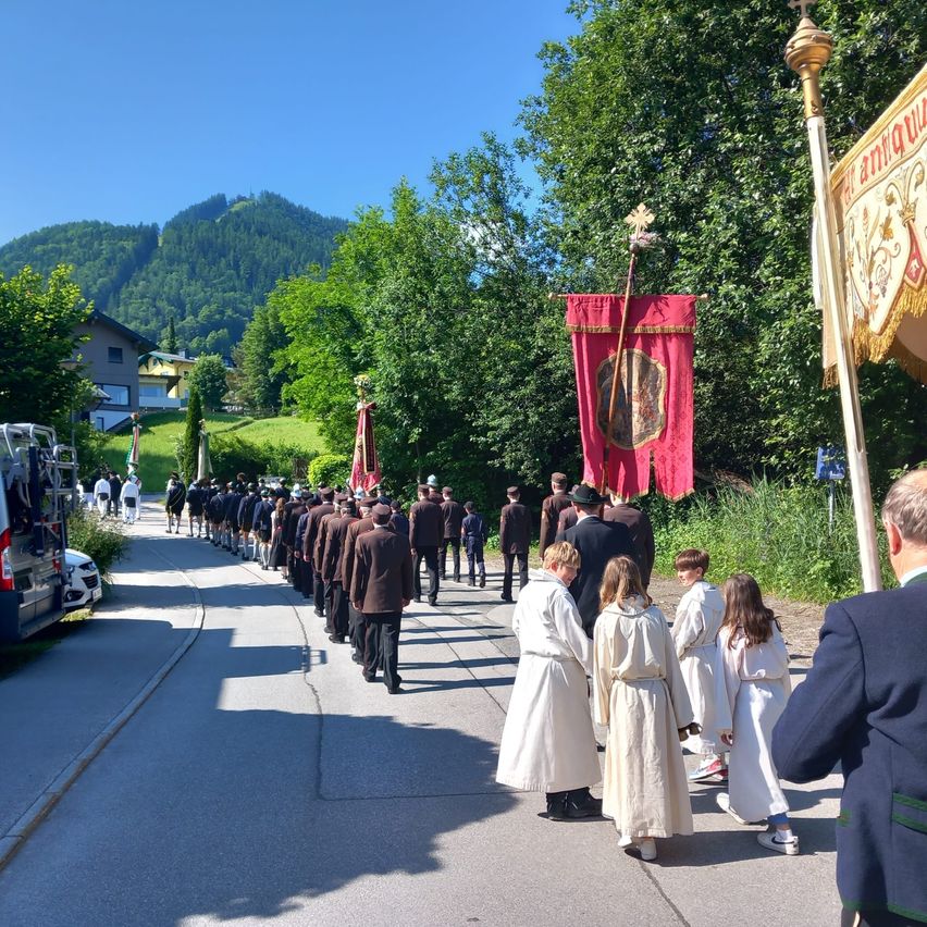 Ein religiöser Umzug findet an einem sonnigen Tag statt, bei dem Menschen in Roben auf der Straße gehen und andere zusehen.