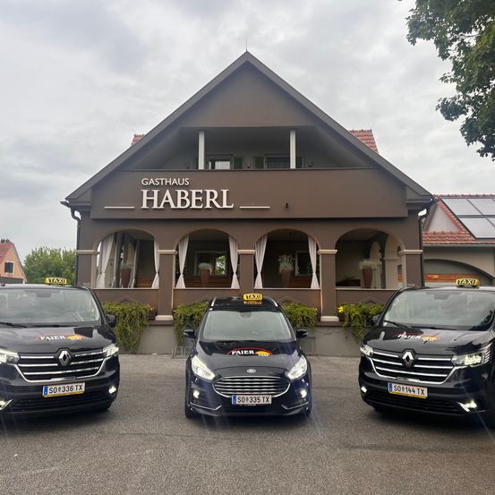 Drei Taxis sind vor dem Gasthaus Haberl geparkt, einem braunen Gebäude mit rotem Dach, weißen Begrenzungen und einer Terrasse. Die Taxis sind schwarz, eines zeigt ein Taxischild auf dem Dach.