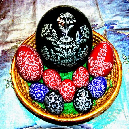 Ein Korb voller dekorativer Ostereier in verschiedenen Farben und mit Blumenmustern, wobei ein schwarzes Ei mit weißen Blumenmustern hervorsticht.