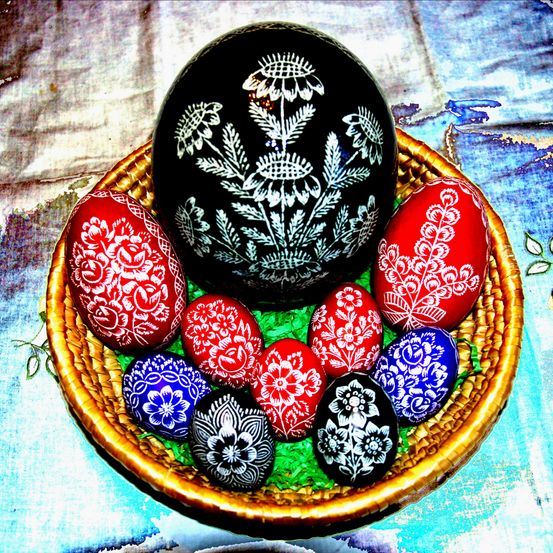 Ein Korb voller dekorativer Ostereier in verschiedenen Farben und mit Blumenmustern, wobei ein schwarzes Ei mit weißen Blumenmustern hervorsticht.