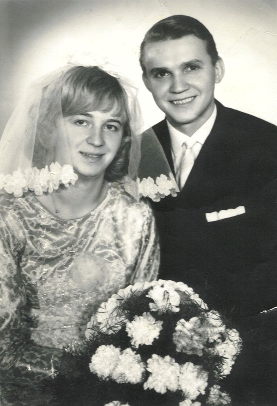 Ein Schwarz-Weiß-Foto eines frisch vermählten Paares. Die Frau trägt ein Spitzenkleid und Schleier. Der Mann ist in einem formellen Anzug gekleidet. Sie lächeln beide.