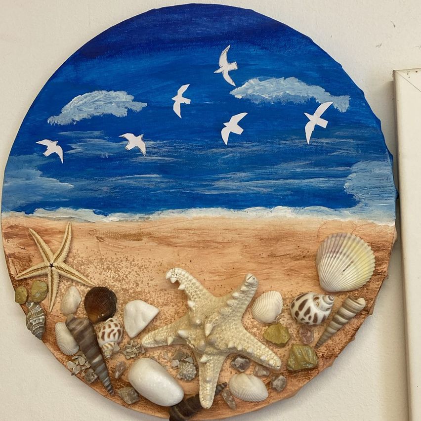 Ein rundes Gemälde zeigt eine Strandszene mit blauem Himmel und weißen Vögeln. Seesterne und verschiedene Muscheln sind am Sand angeordnet.