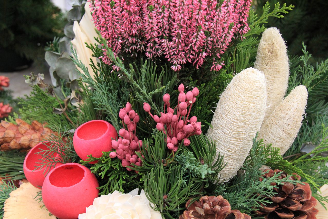 Eine Nahaufnahme einer Blumenarrangement mit rosa und weißen Blumen, grünen Blättern und roten dekorativen Schalen. Das Arrangement umfasst eine Mischung aus natürlichen und künstlichen Elementen.