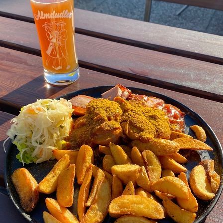Ein Teller mit knusprigen Pommes und einem Beilagensalat sowie einem Glas Bier steht auf einem Holztisch.