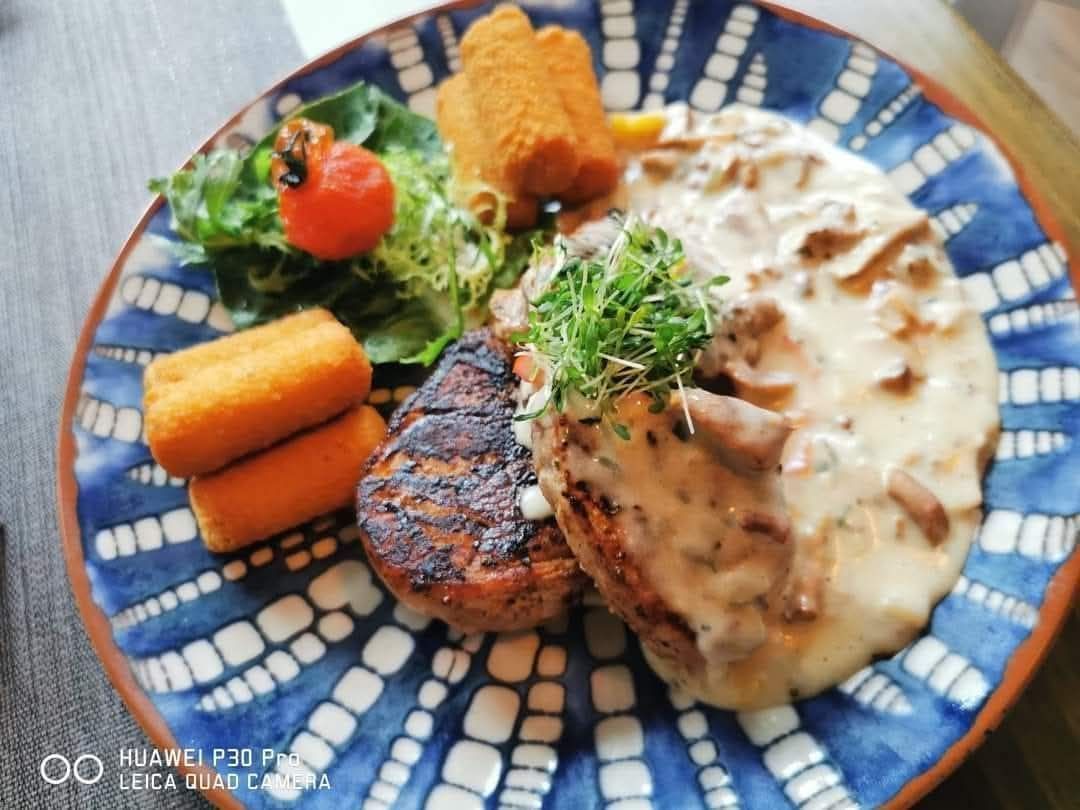 Ein blau und weiß gemusterter Teller mit zwei gegrillten Steaks, cremiger Pilzsauce, grünem Salat und zwei frittierten Gemüsestücken.