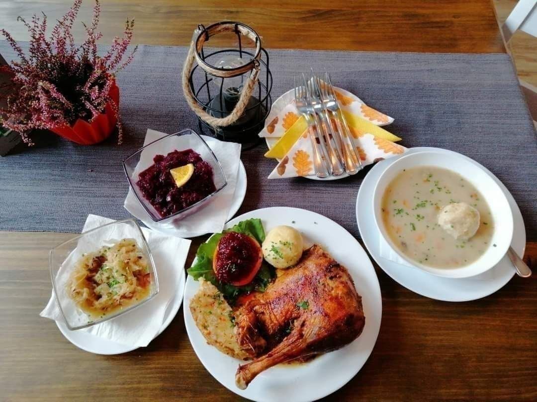 A wooden table set with plates of food, including a roasted chicken, soup, and side dishes. A lantern and a potted plant add rustic charm.