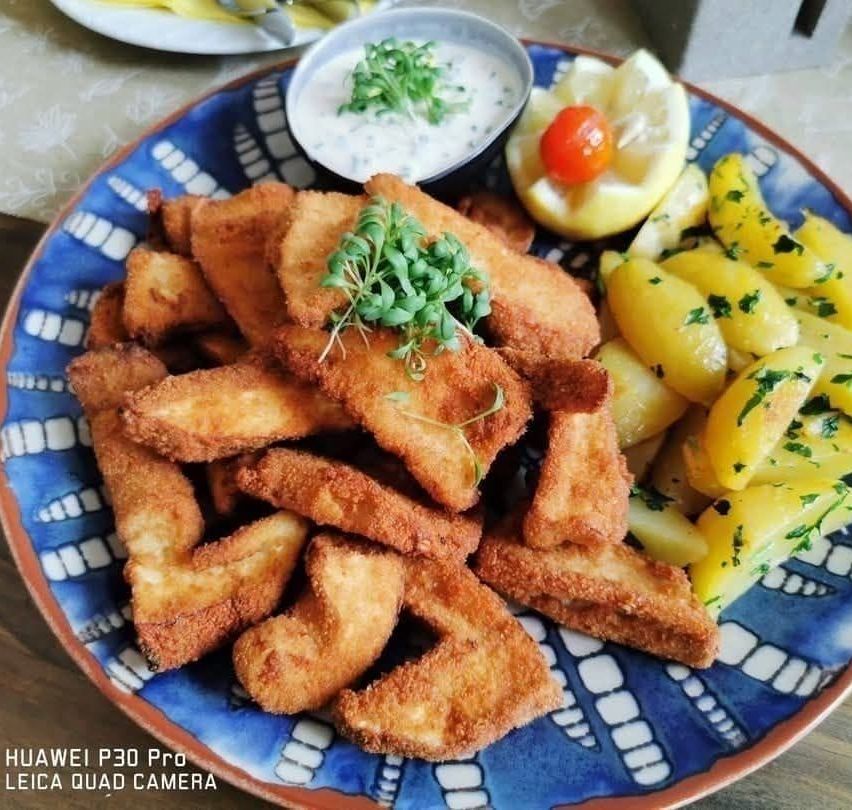 A plate of crispy fried fish pieces with a side of lemon wedges and a bowl of creamy dip.