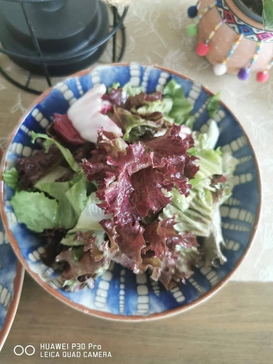A blue and white patterned bowl filled with a fresh salad of red and green lettuce leaves with a creamy dressing.