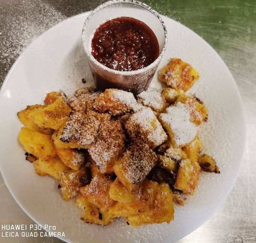 A plate with fried banana slices topped with brown sugar and cinnamon, accompanied by a small cup of red sauce.