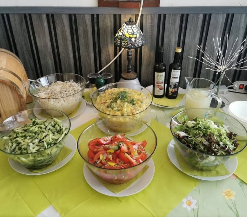 Ein Tisch mit verschiedenen Salatschüsseln, einer Karaffe mit Dressing und zwei Flaschen Öl. Eine Lampe und Dekorationsartikel sind ebenfalls vorhanden.