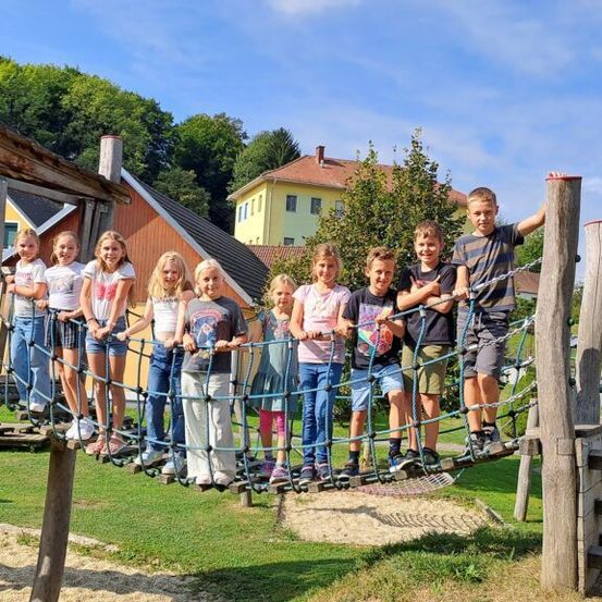 Eine Gruppe von Kindern steht auf einem Kletternetz in einem Spielplatz und posiert für ein Foto.