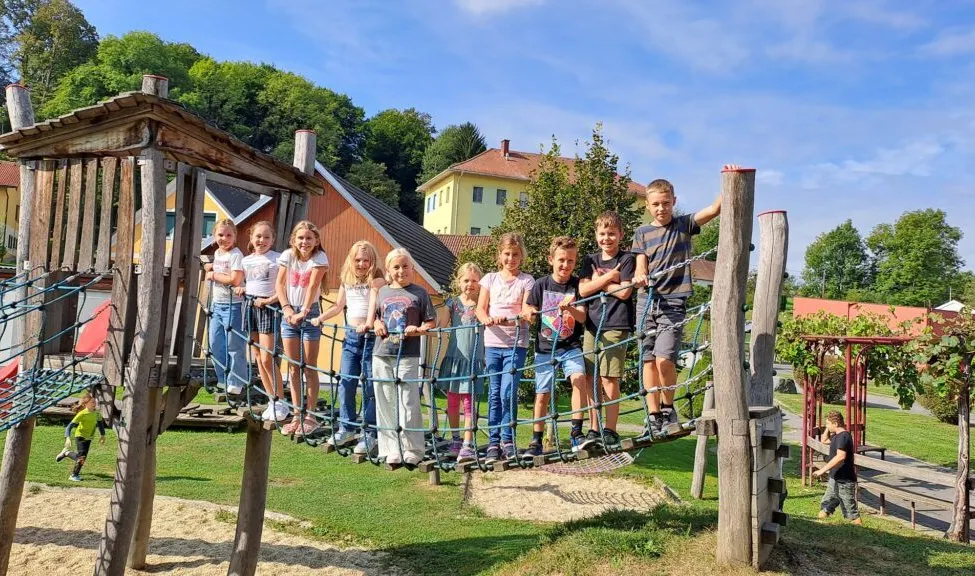 Eine Gruppe von Kindern steht auf einem Kletternetz in einem Spielplatz und posiert für ein Foto.