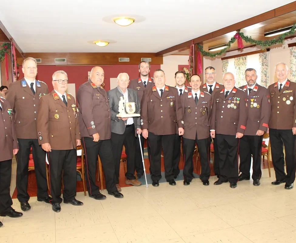 Eine Gruppe von Männern in Militäruniformen steht in einem Raum. Einer hält eine Trophäe. Hinter ihnen schmückt eine Weihnachtsgirlande die Wand.
