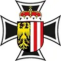 Ein heraldisches Emblem mit einem schwarzen Eisernen Kreuz und einem zentralen Schild, der einen gelben Adler auf schwarzem Hintergrund und einen rot-weiß gestreiften Abschnitt zeigt. Oben auf dem Schild befindet sich eine Krone.