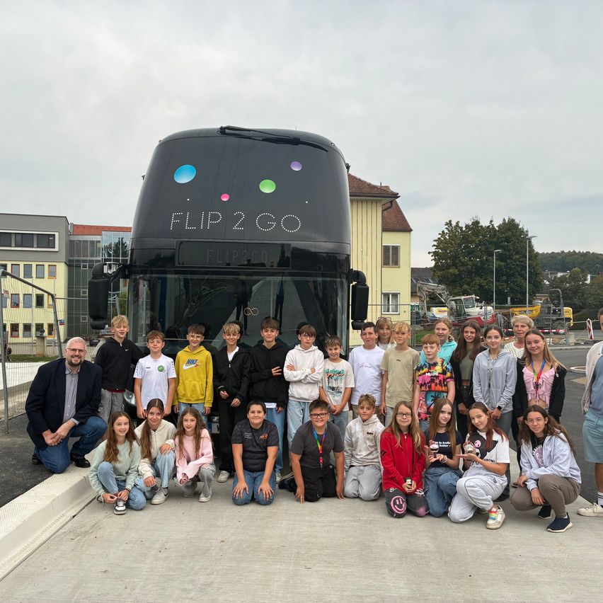 Eine Gruppe von Menschen, einschließlich Kindern, posiert für ein Foto vor einem schwarzen Bus mit den Worten Flip 2 Go darauf.