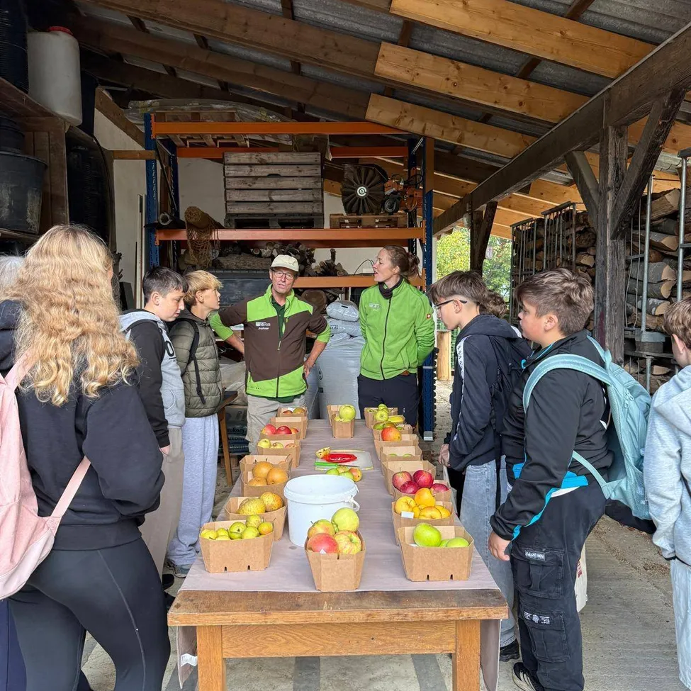Eine Gruppe von Menschen steht um einen Tisch herum, der mit verschiedenen Früchten gefüllt ist, in einem Lagerraum.