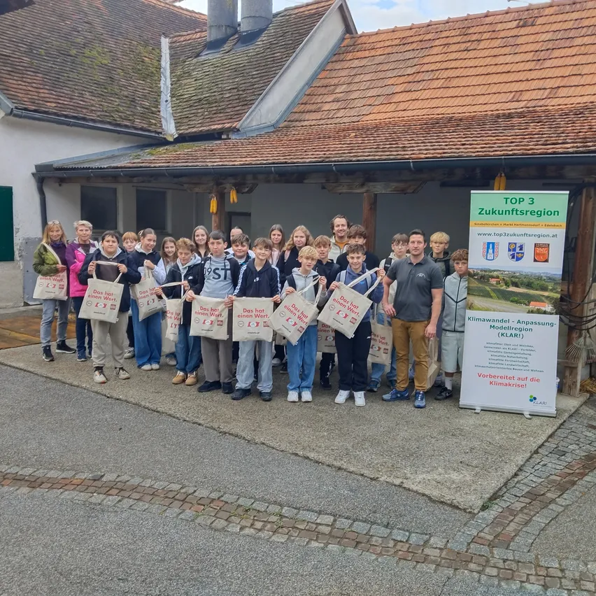 Eine Gruppe von Menschen steht vor einem Gebäude, hält Taschen und lächelt für ein Foto.