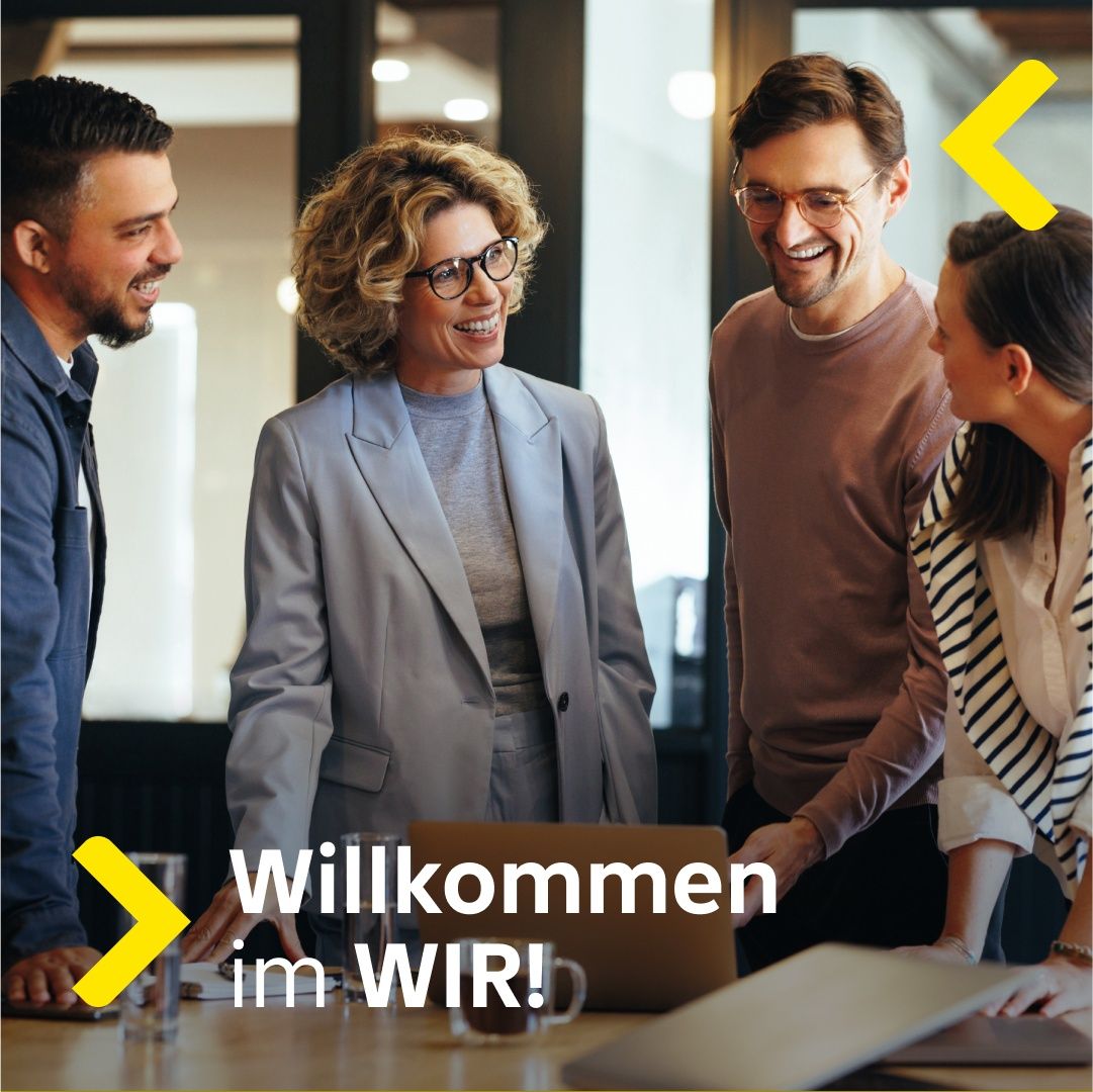Vier Menschen stehen um einen Tisch mit einem Laptop herum, lächeln und interagieren. Eine Frau in einer grauen Blazerjacke steht in der Mitte, mit einem Mann mit Brille rechts von ihr und einer weiteren Frau in Streifen links von ihr. Der Text lautet 'Willkommen im WIR!' mit einem gelben Pfeil nach links.