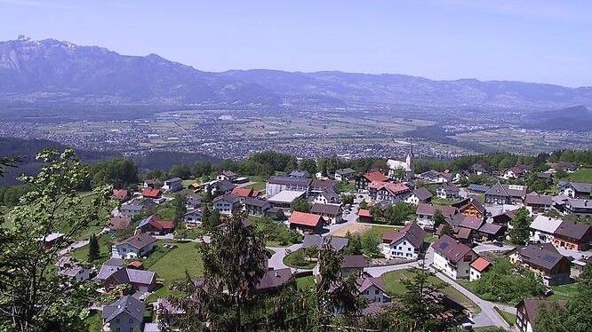 Ein malerisches Dorf in den Bergen mit rotgedeckten Häusern, einer Kirche und üppigem Grün.