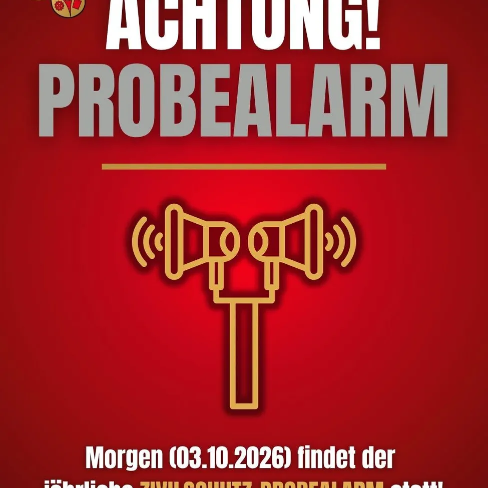 Ein roter Plakat mit einem goldenen Alarmsymbol und Text auf Deutsch. Es steht 'ACHTUNG! PROBEALARM' und 'Morgen (03.10.2026) findet der jahrliche ZIVILSCHUTZ-PROBEALARM statt!'