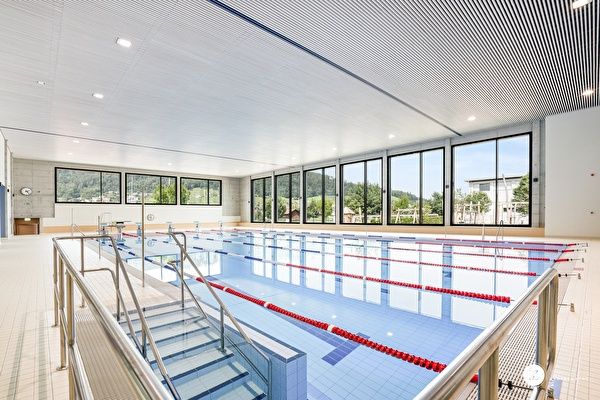 Ein Hallenschwimmbad mit mehreren Bahnen und Glaswänden, mit Blick auf die Außenlandschaft.