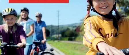 Ein Plakat für eine Familienradwanderung am 3. Mai 2026 von 10 bis 17 Uhr. Vier Personen fahren auf einer Straße mit Fahrrädern. Ein Mädchen lächelt vorne, und andere folgen. Bäume und Häuser im Hintergrund.