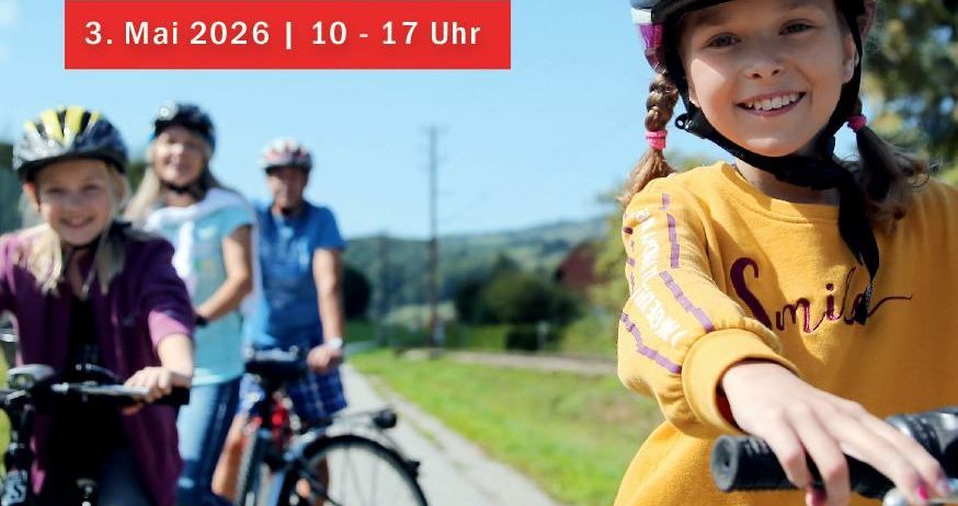 Ein Plakat für eine Familienradwanderung am 3. Mai 2026 von 10 bis 17 Uhr. Vier Personen fahren auf einer Straße mit Fahrrädern. Ein Mädchen lächelt vorne, und andere folgen. Bäume und Häuser im Hintergrund.