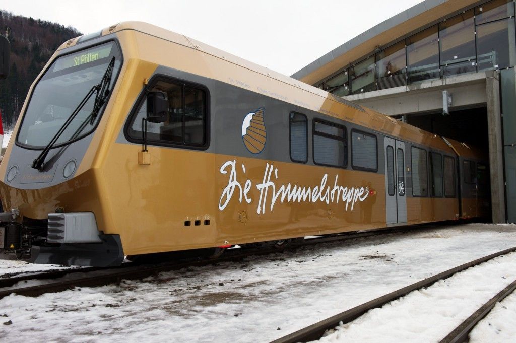 Ein goldener Zug mit der Aufschrift 'Die Himmelstreppe' steht auf einem verschneiten Bahngleis unter einer überdachten Plattform.