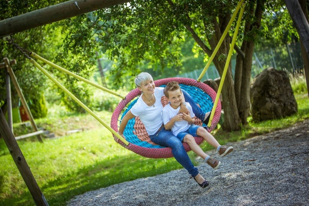 Eine Frau und ein Junge genießen eine Fahrt auf einer bunten Schaukel im Park. Sie lächeln und wirken fröhlich.