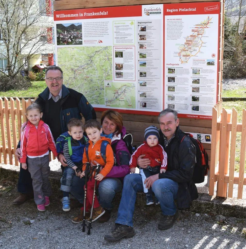 Eine Familie mit sechs Mitgliedern, darunter zwei Erwachsene und vier Kinder, posiert für ein Foto vor einem Schild, das 'Willkommen in Frankenfels!' steht. Sie alle lächeln und scheinen ihren Tag zu genießen.