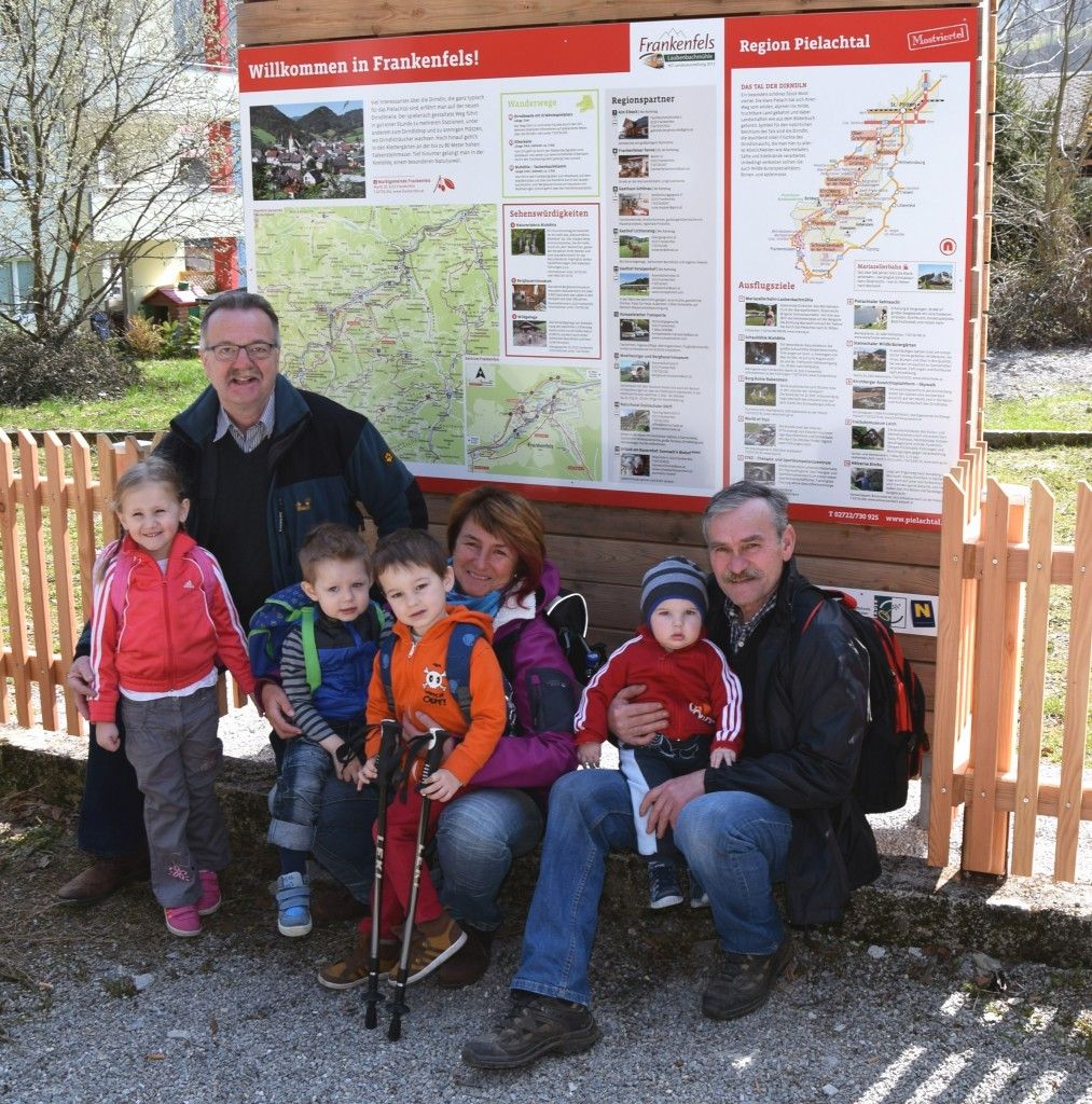 Eine Familie mit sechs Mitgliedern, darunter zwei Erwachsene und vier Kinder, posiert für ein Foto vor einem Schild, das 'Willkommen in Frankenfels!' steht. Sie alle lächeln und scheinen ihren Tag zu genießen.