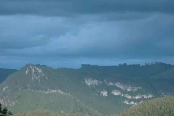 Ein Gebirgszug mit dichter Vegetation und felsigen Bereichen unter einem bewölkten Himmel.
