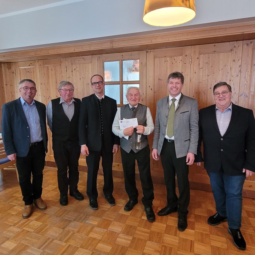 Sechs Männer in Anzügen stehen in einem Raum mit Holzwänden. Ein Mann hält ein Papier. Sie tragen alle eine Brille.