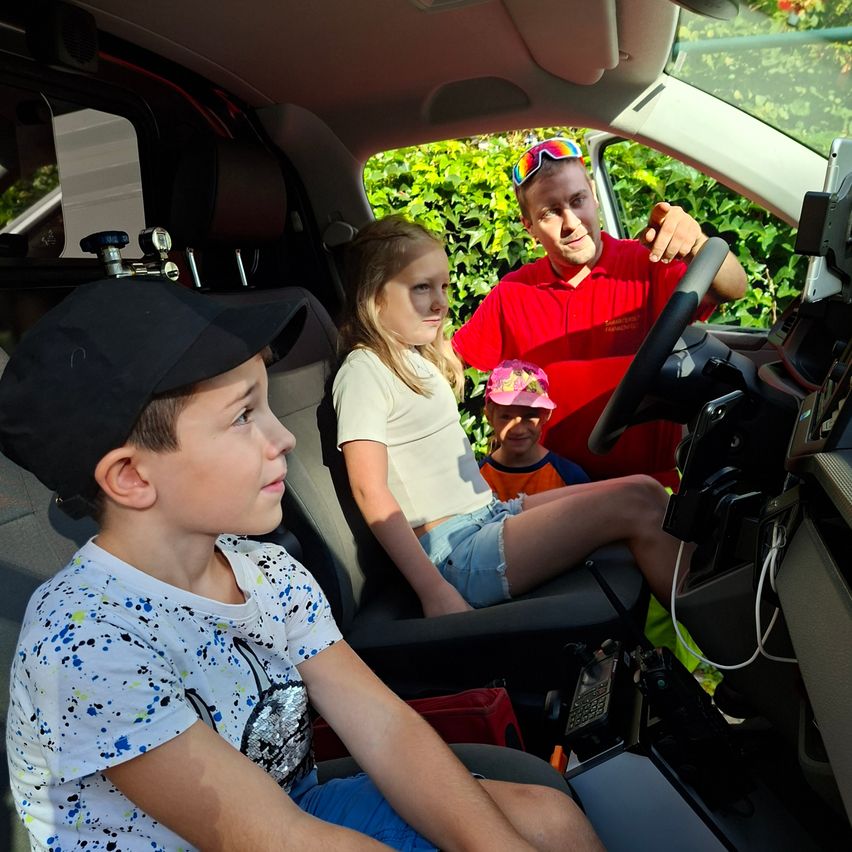 Ein Mann in einem roten Hemd fährt ein Fahrzeug, während ein junger Junge und ein Mädchen auf den Vordersitzen sitzen und ein Kleinkind auf dem Schoß des Mannes sitzt.