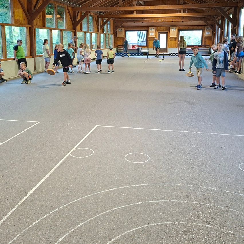 Eine Gruppe von Kindern spielt Discgolf in einem großen, offenen Raum mit Holzbalken und großen Fenstern.