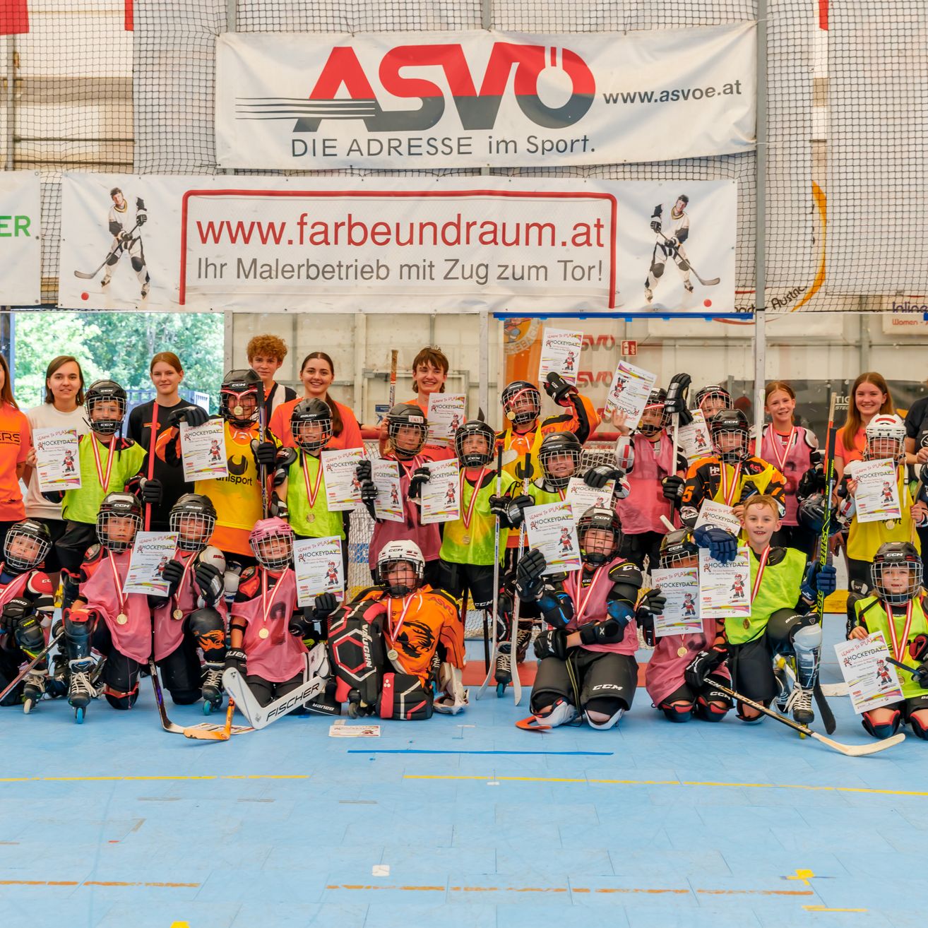 Eine Gruppe junger Hockeyspieler mit ihren Trainern posiert für ein Foto in einer Eishalle und hält Urkunden und Schläger in den Händen.