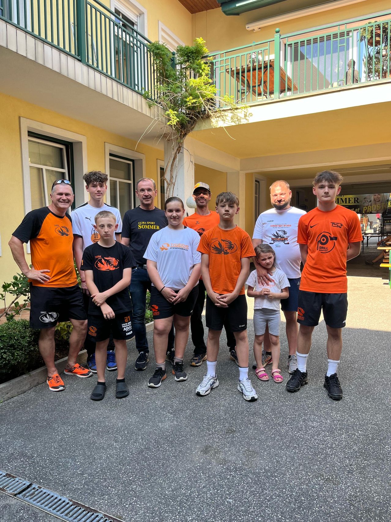 Eine Gruppe von Menschen in passenden orangefarbenen und weißen Trikots und Shorts posiert für ein Foto vor einem Gebäude.