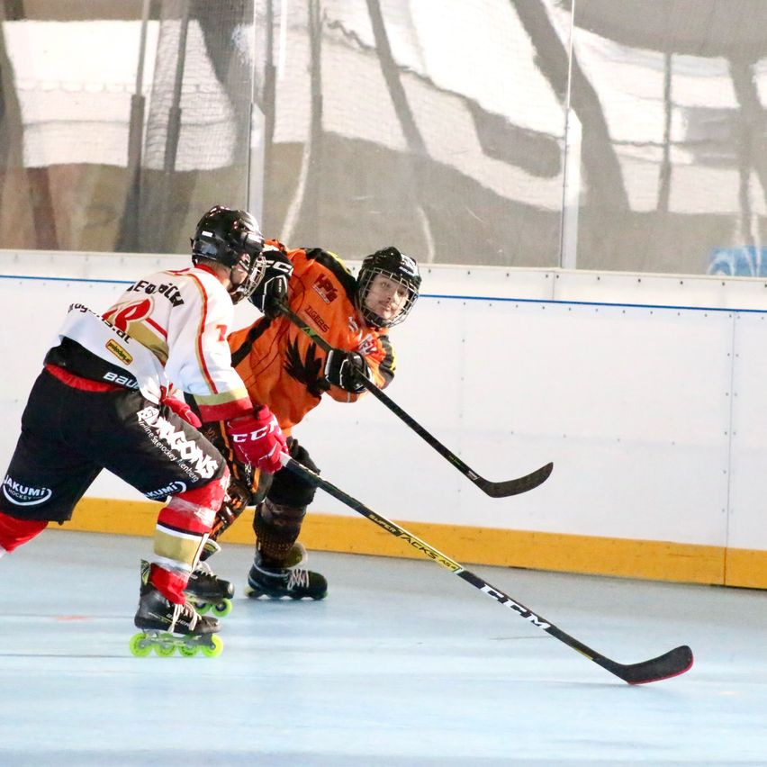 Zwei Eishockeyspieler auf einer Eishalle in Helmen und Schlittschuhen, einer mit einem Hockeyschläger.