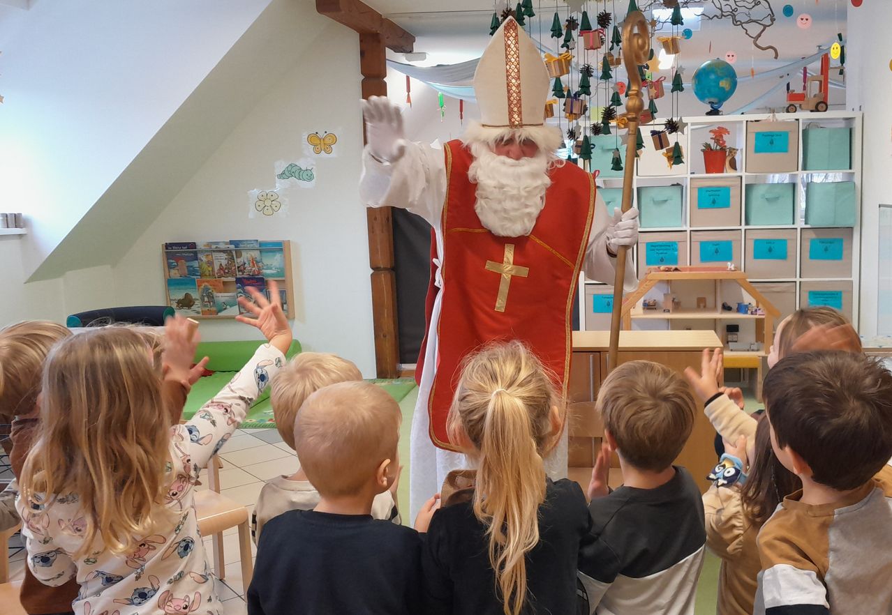 Eine als Weihnachtsmann verkleidete Person unterhält eine Gruppe von Kindern in einem Klassenzimmer mit festlicher Dekoration und Umgebung.