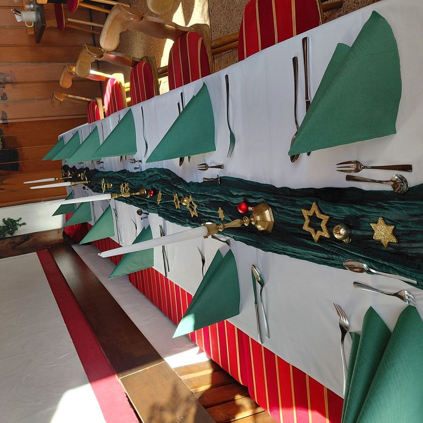 A long table set for a special occasion with green napkins, silverware, and a decorative green runner with ornaments.